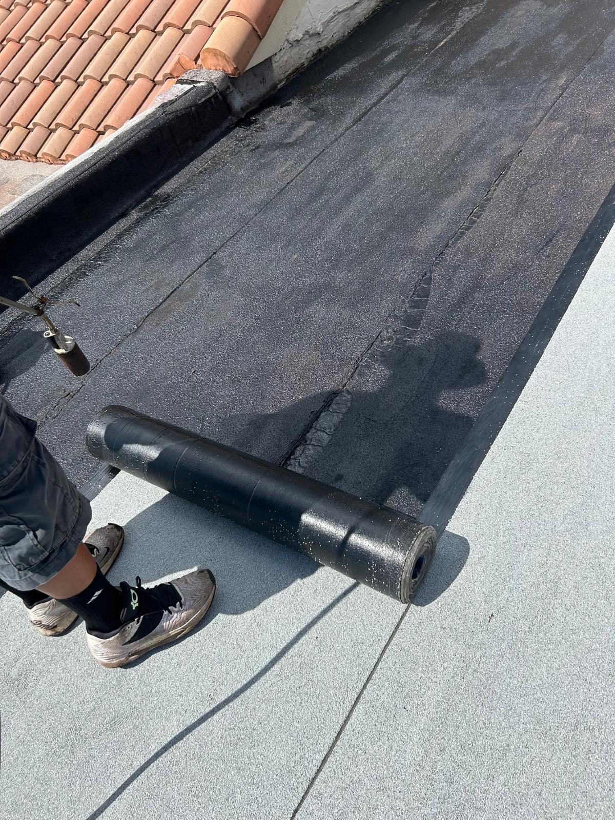 Roll of modified bitumen membrane on a flat roof beside a torch tool