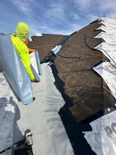 Roofer in safety gear tearing off old shingles and drying in the deck